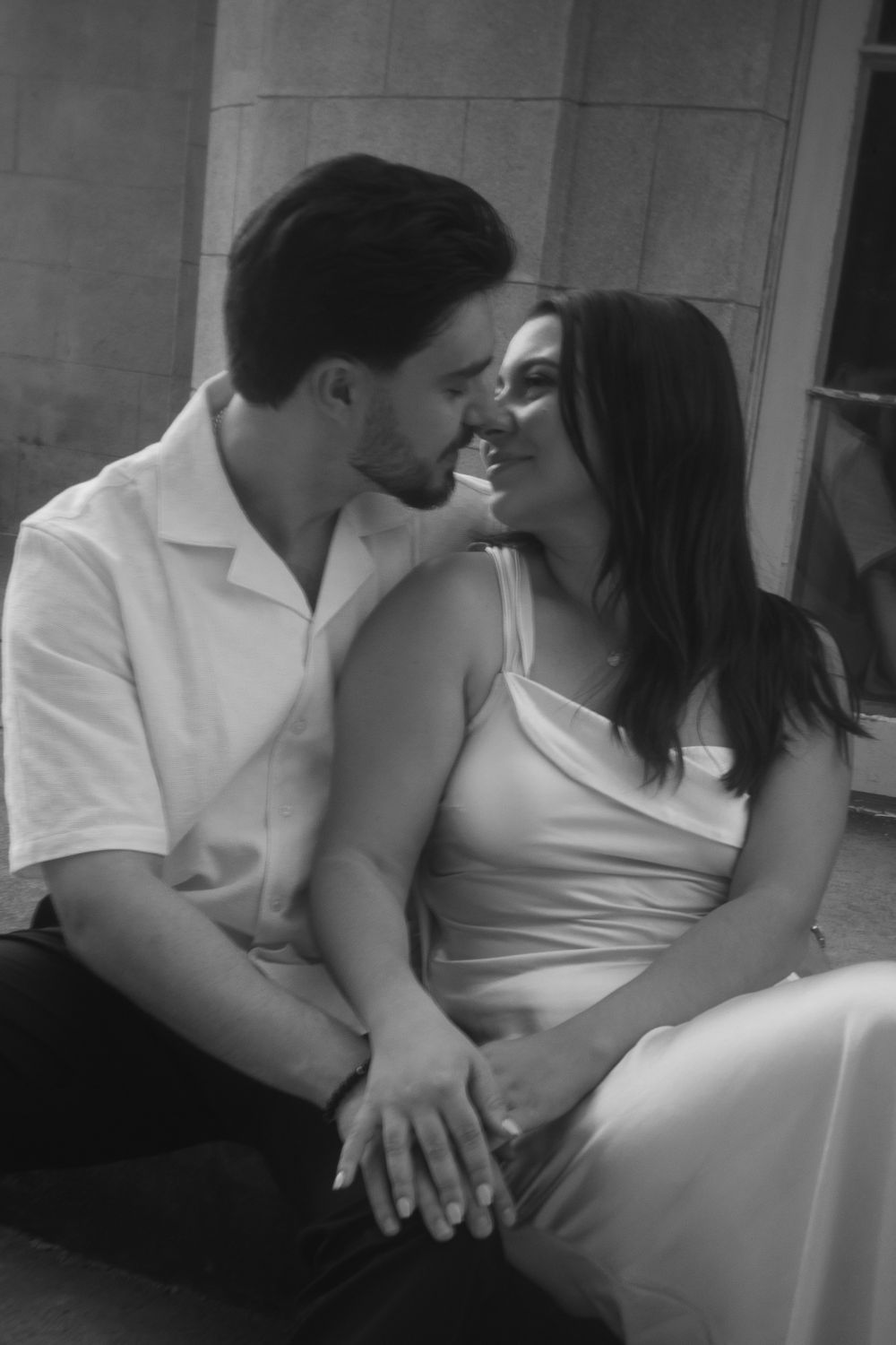 A romantic black and white portrait of a couple in light colored clothing sitting close together in an intimate moment.