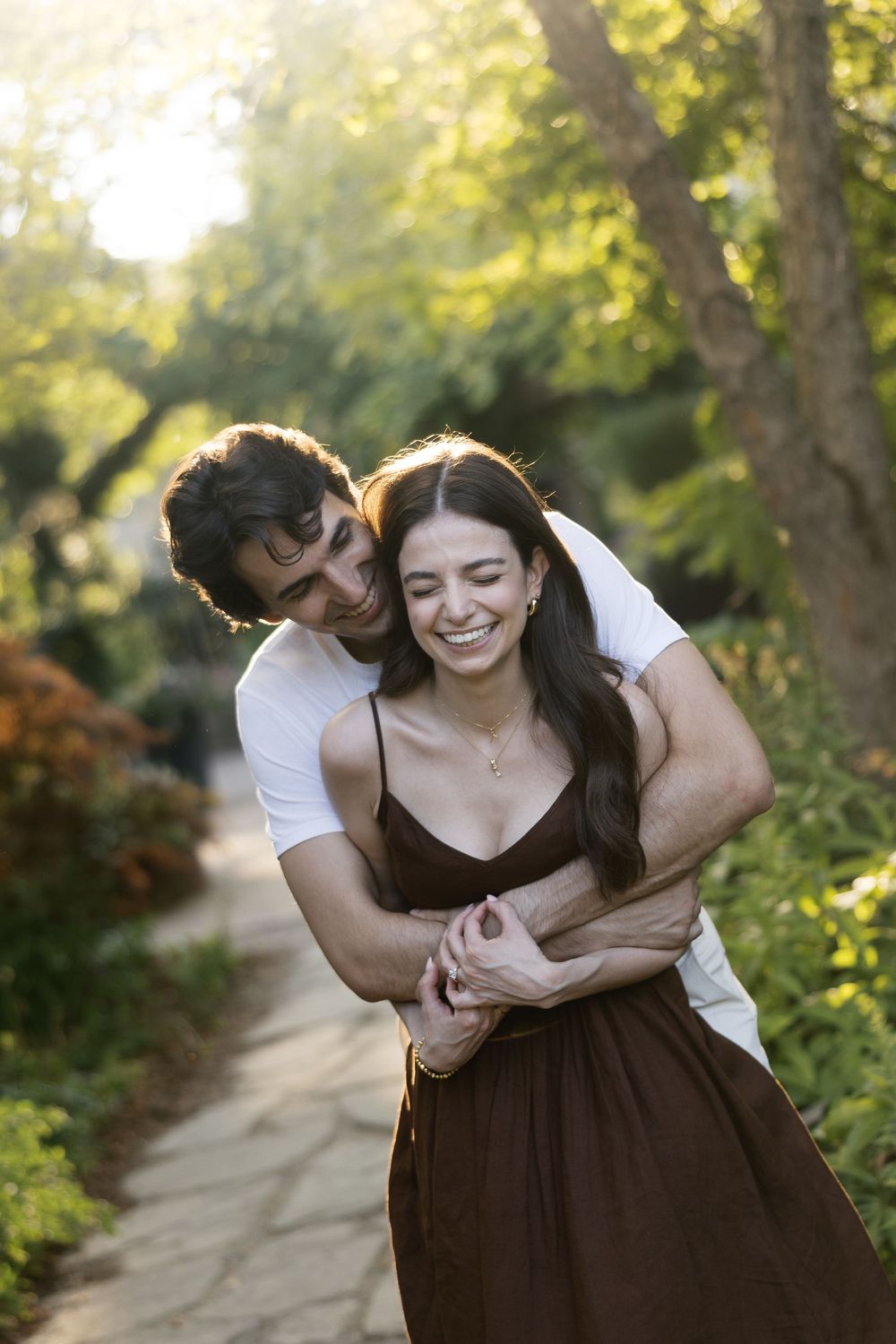 Romantic outdoor couple session showing a tender embrace on a sunlit garden path.
