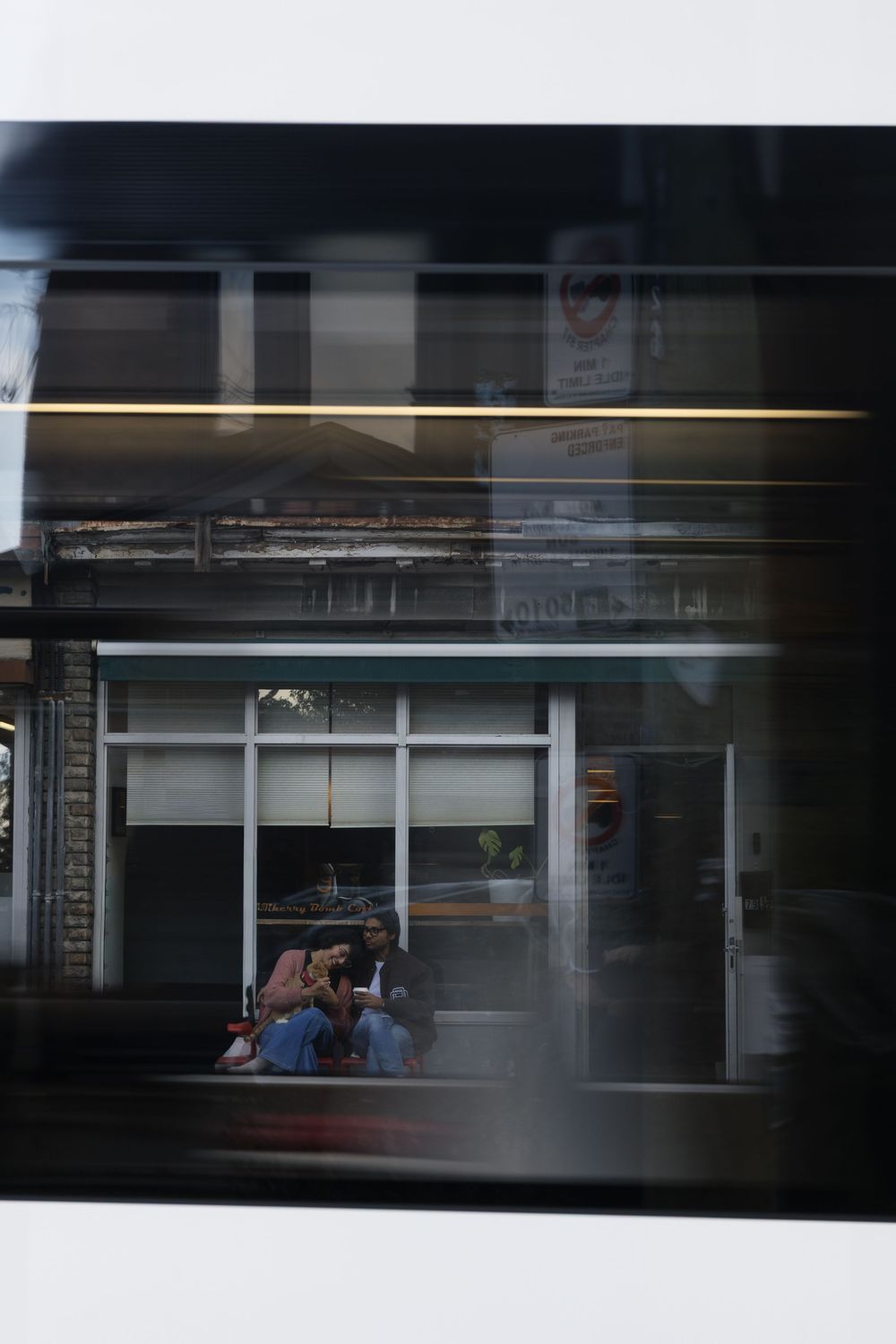 Through a window reflection, people sit at a storefront while light streaks across the dark glass surface.
