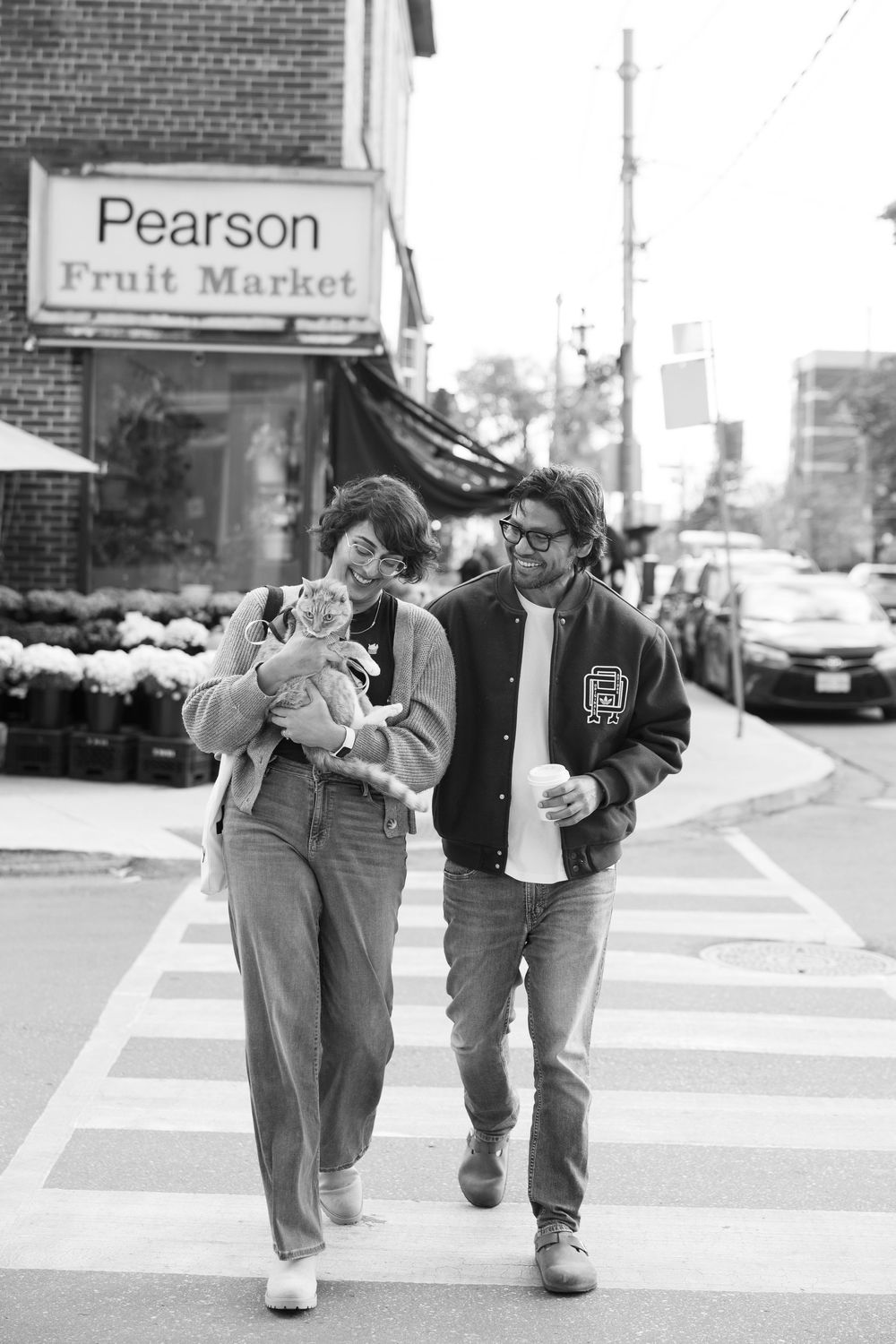 A couple walking hand in hand down a city sidewalk past storefronts in black and white photography.
