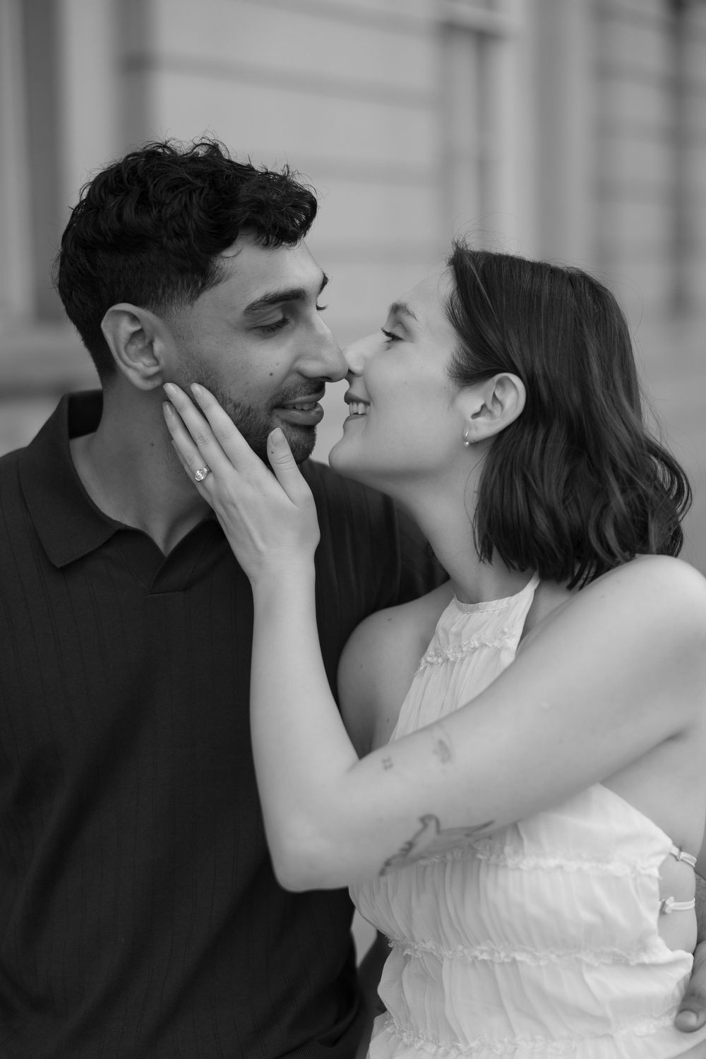 Black and white photo of a couple sharing a romantic moment, woman tenderly holding mans face as they lean in close.