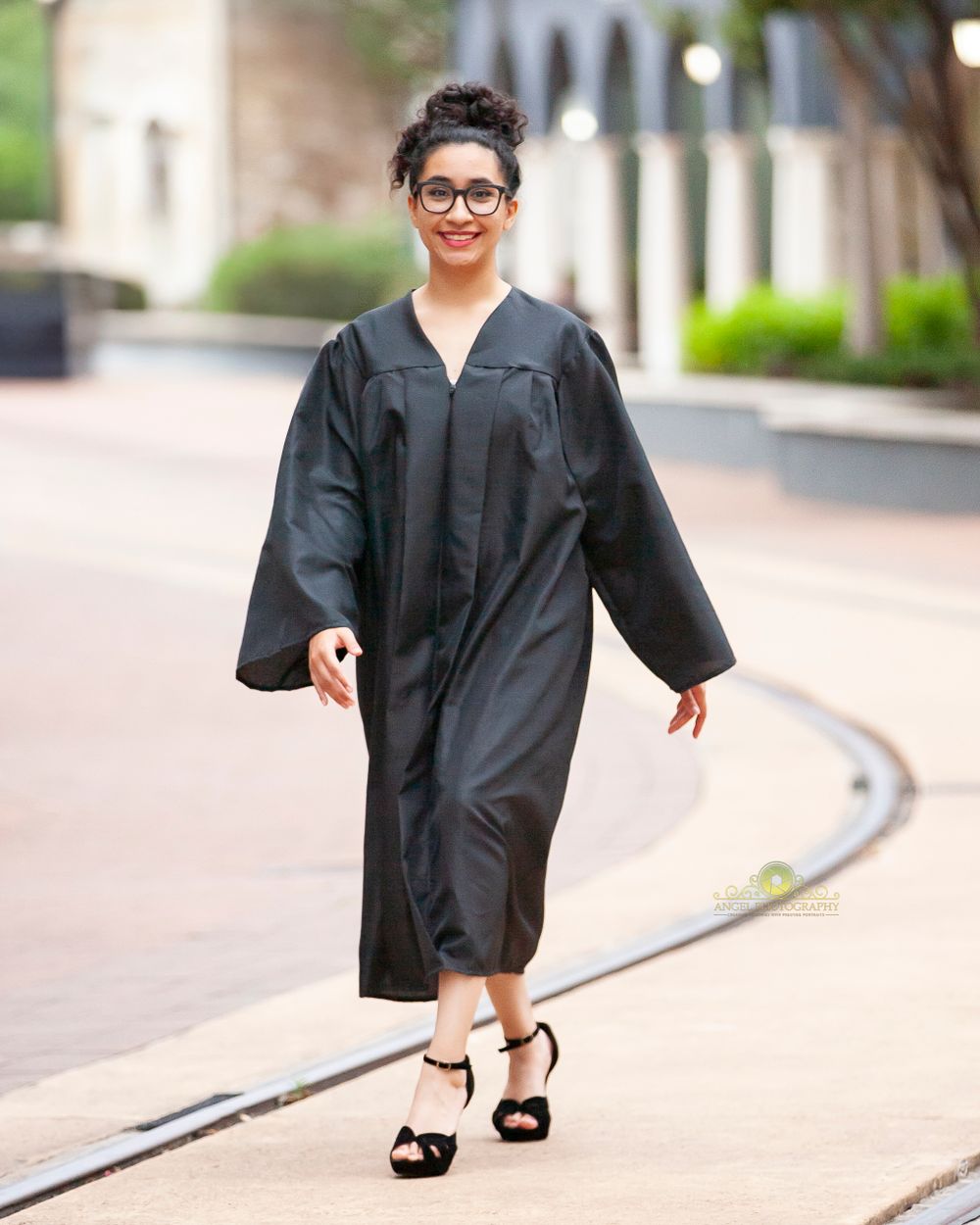 Graduate walking confidently in black graduation gown and heels along curved path.