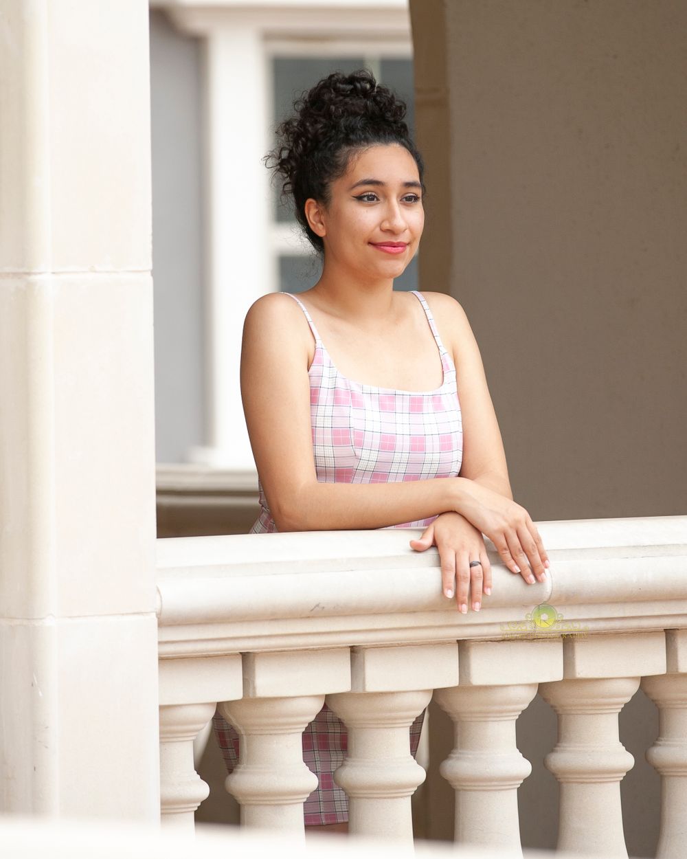 Portrait at balcony railing wearing pink plaid summer dress.