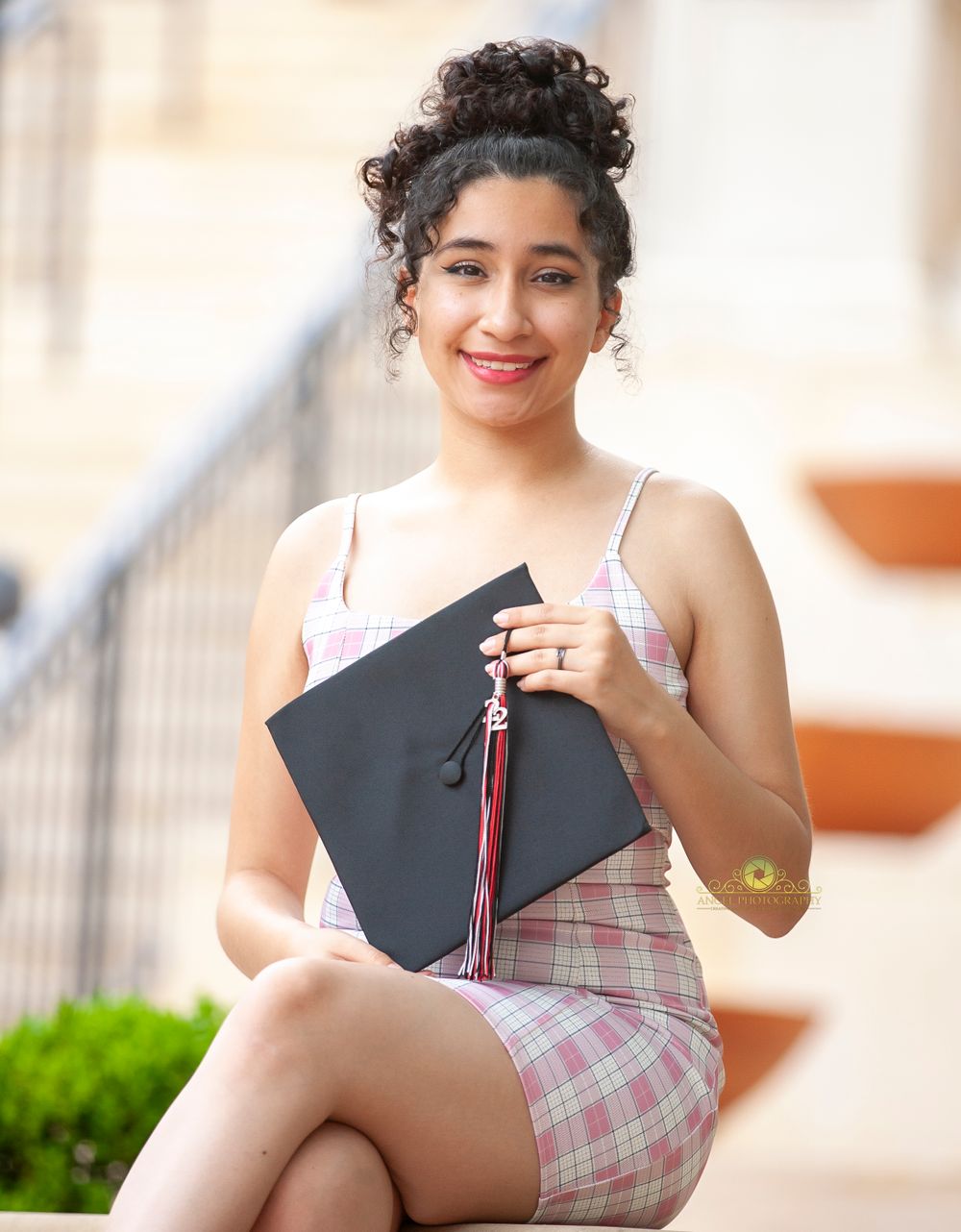 Graduate holding cap and tassel while wearing pink plaid dress.