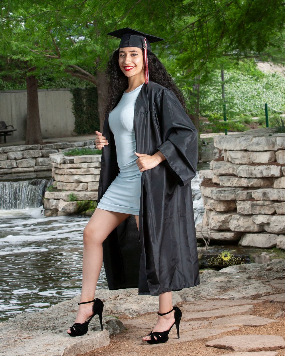 Graduate in academic regalia strikes a pose by a decorative water feature.