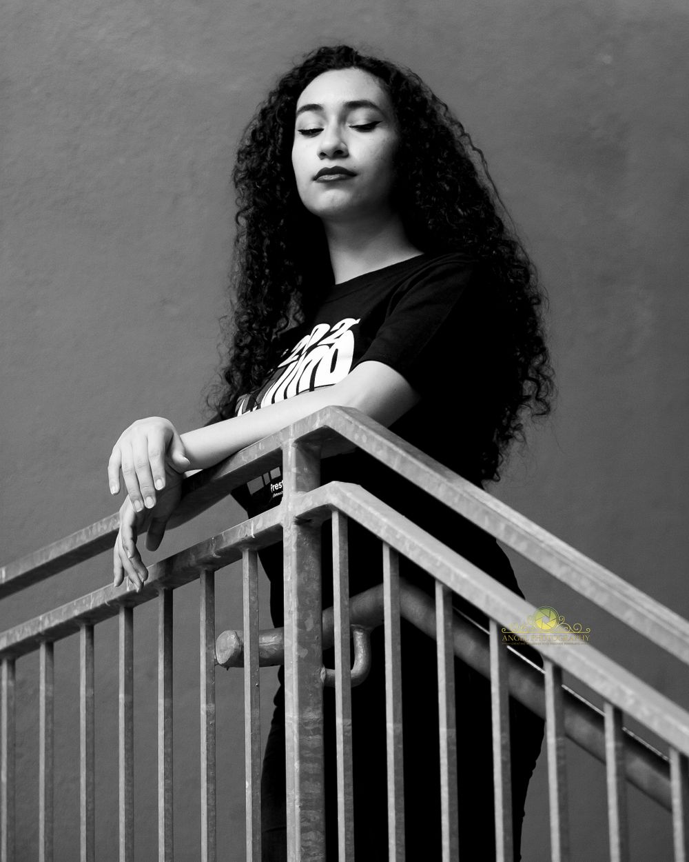 Black and white portrait of person with curly hair leaning on metal railing.