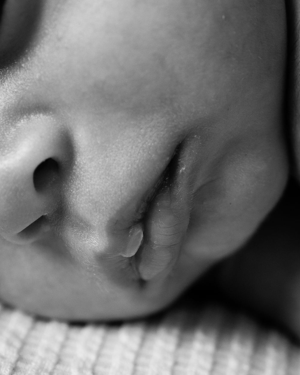 Close-up black and white photo of a sleeping newborn baby's face on a soft textured blanket.