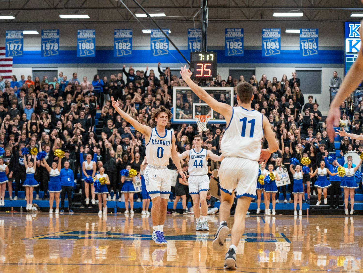 Basketball player making dramatic shot in crowded gymnasium with enthusiastic fans.
