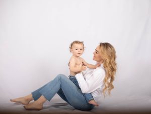 mamma som sitter på golvet med sitt barn i knät. mamman kollar på barnet och barnet kollar in i kameran.
