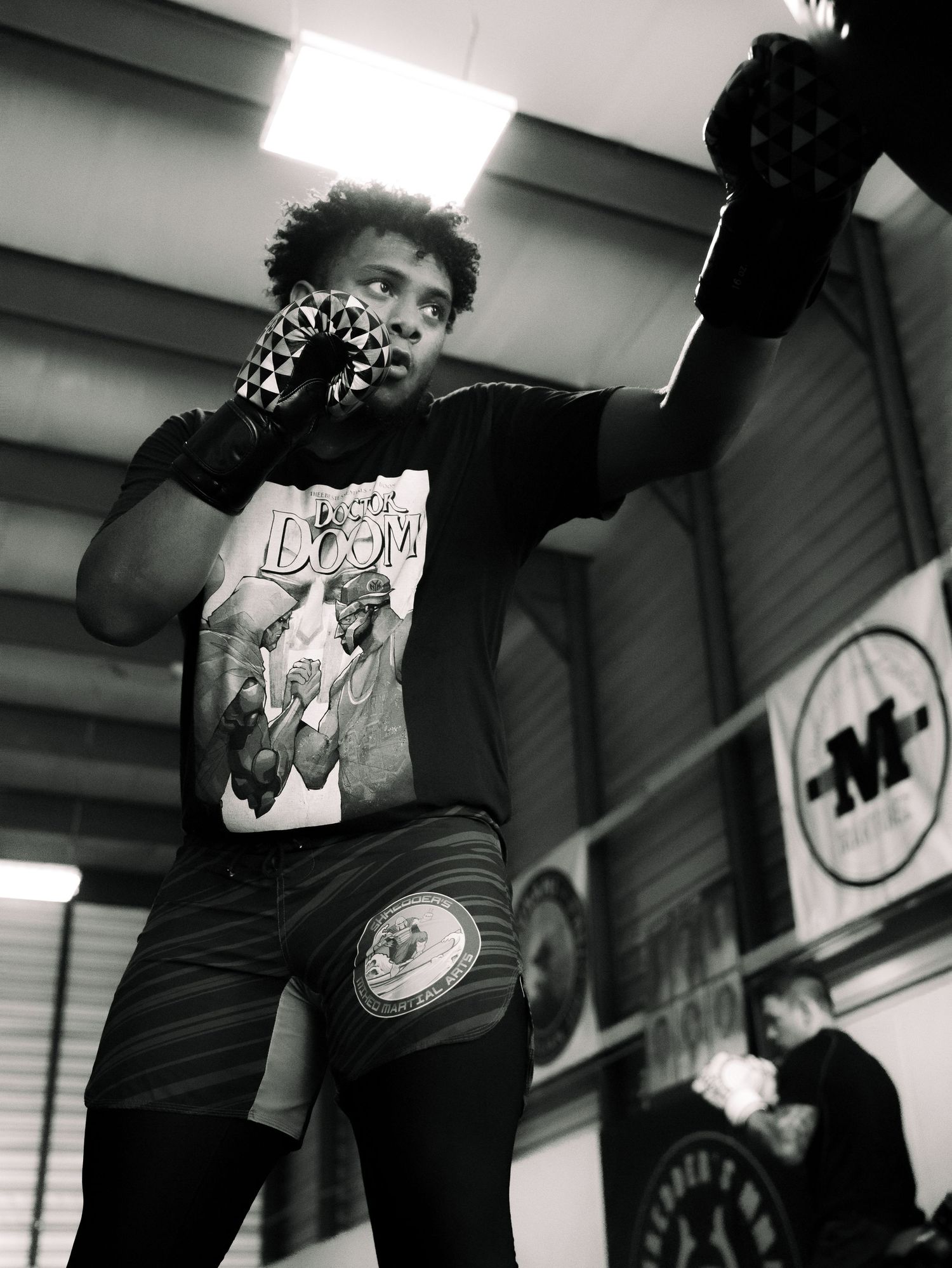 A person in a graphic t-shirt and face mask poses energetically in a gym setting.