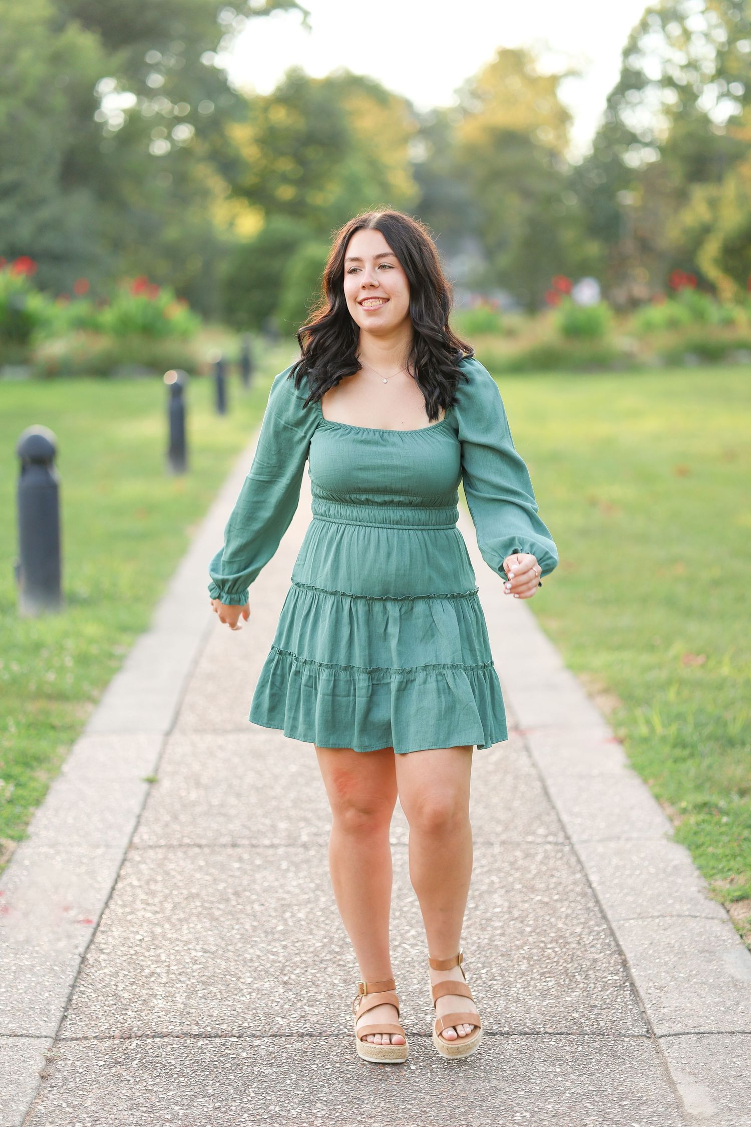 A person walks confidently down a garden path wearing a flowy teal dress and sandals.