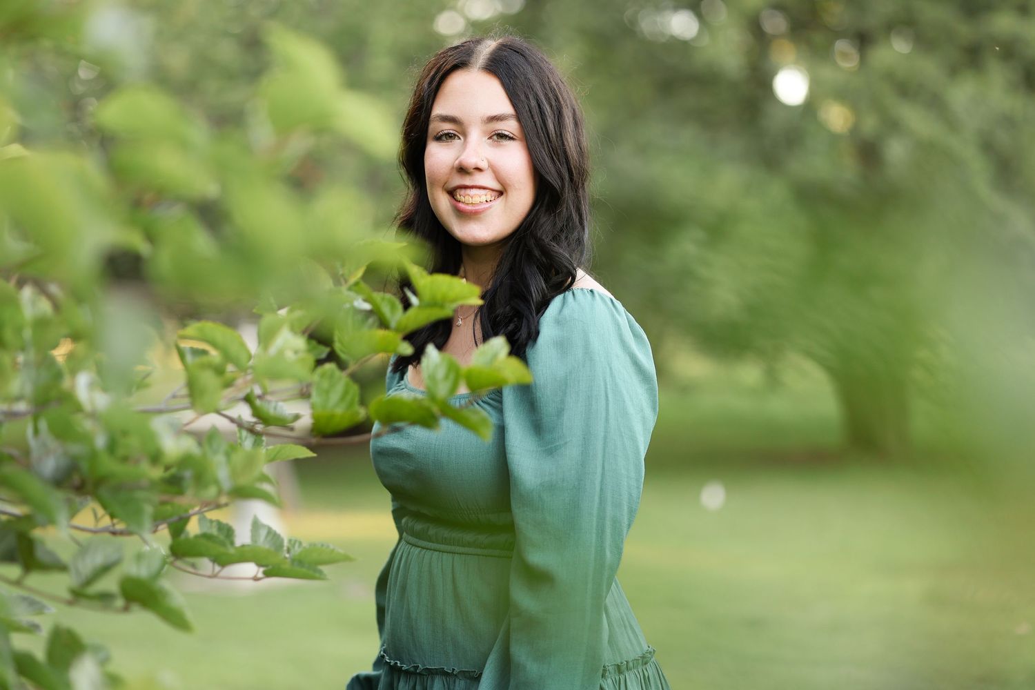 Casual outdoor portrait in a green dress surrounded by leaves in a garden setting.