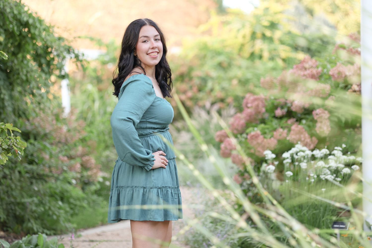 Woman in teal dress posing in a flowery garden setting with natural bokeh background.