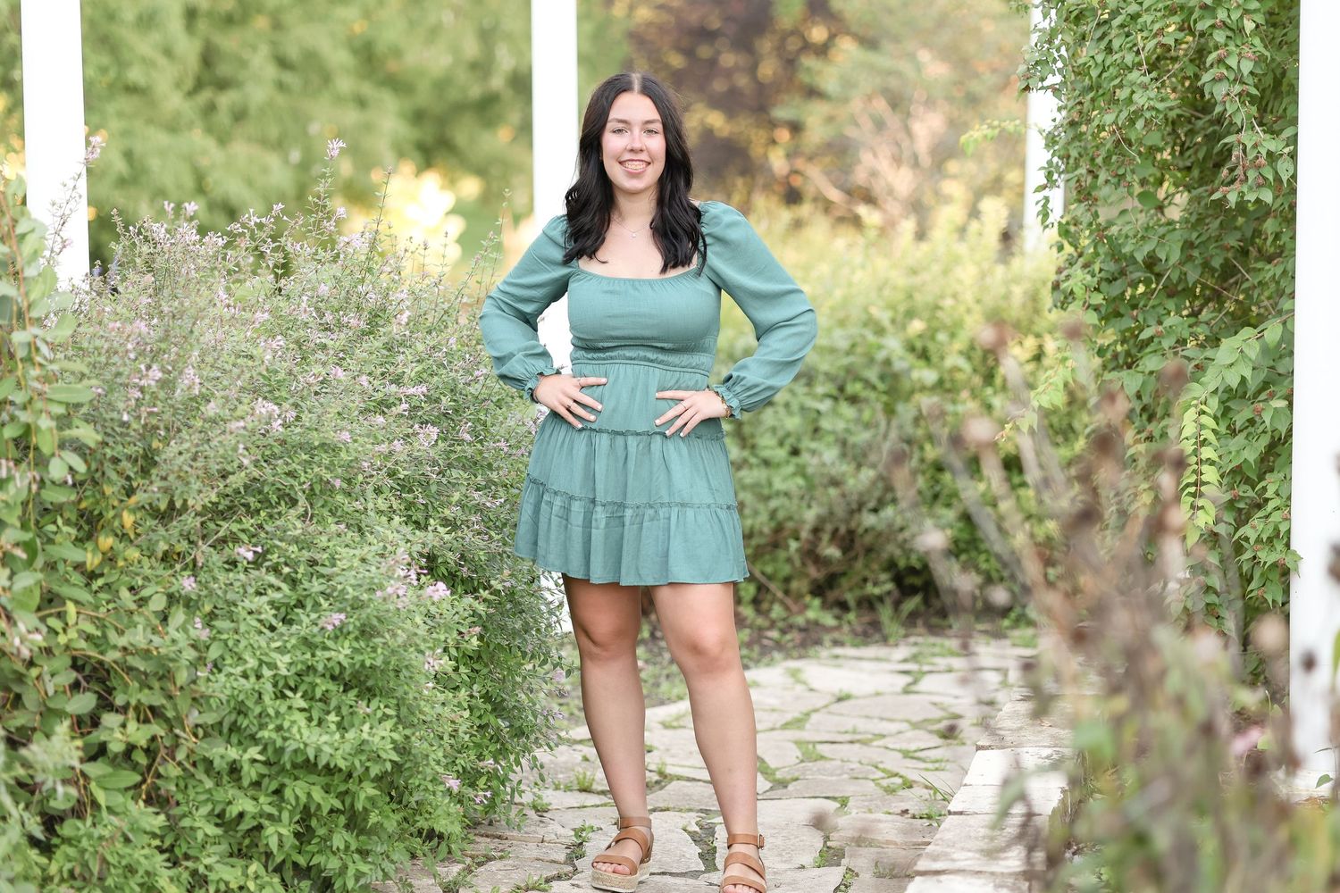 Full length portrait in green dress standing on stone pathway in garden setting.