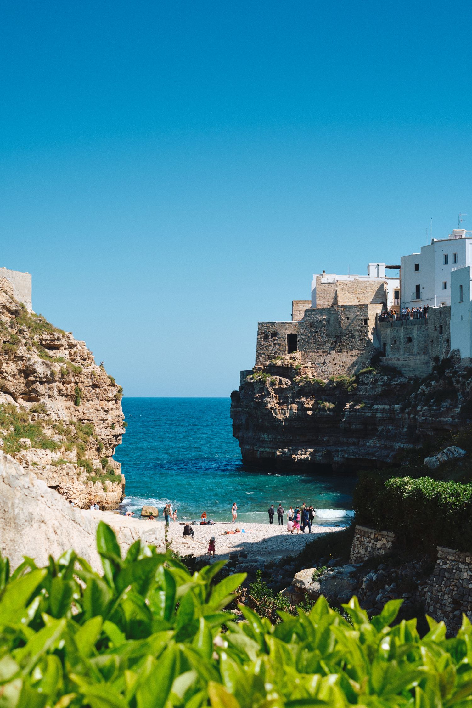 White buildings perched on limestone cliffs above a turquoise beach cove in Italy.