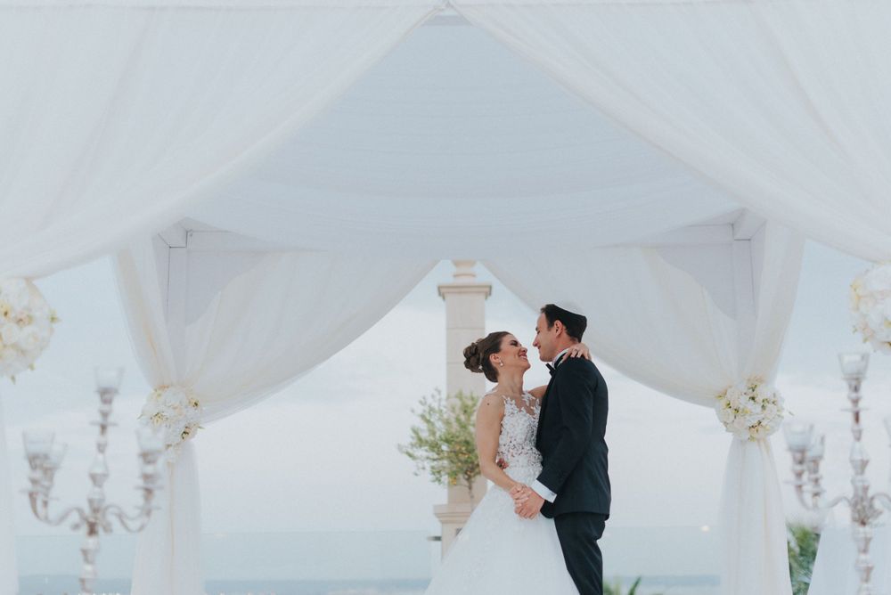 Wedding couple embracing under elegant white canopy with floral decorations and soft lighting.