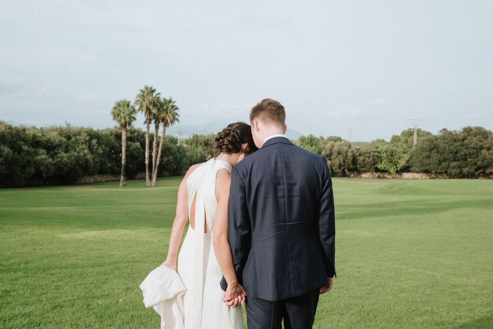 Wedding couple walking hand in hand on lush golf course with palm trees.