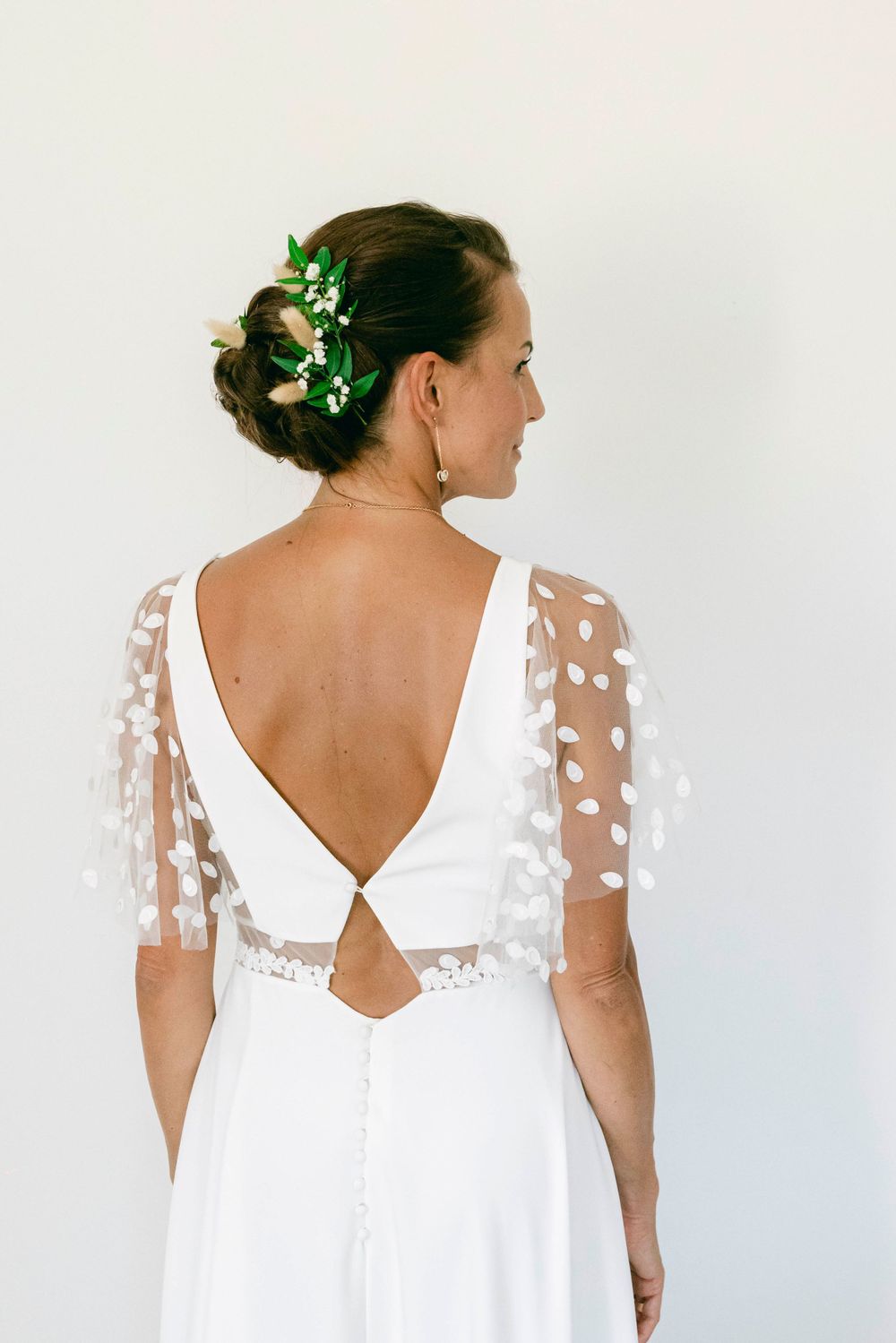 Back view of wedding dress showing v-cut design with sheer polka dot sleeves and green hair accessories.