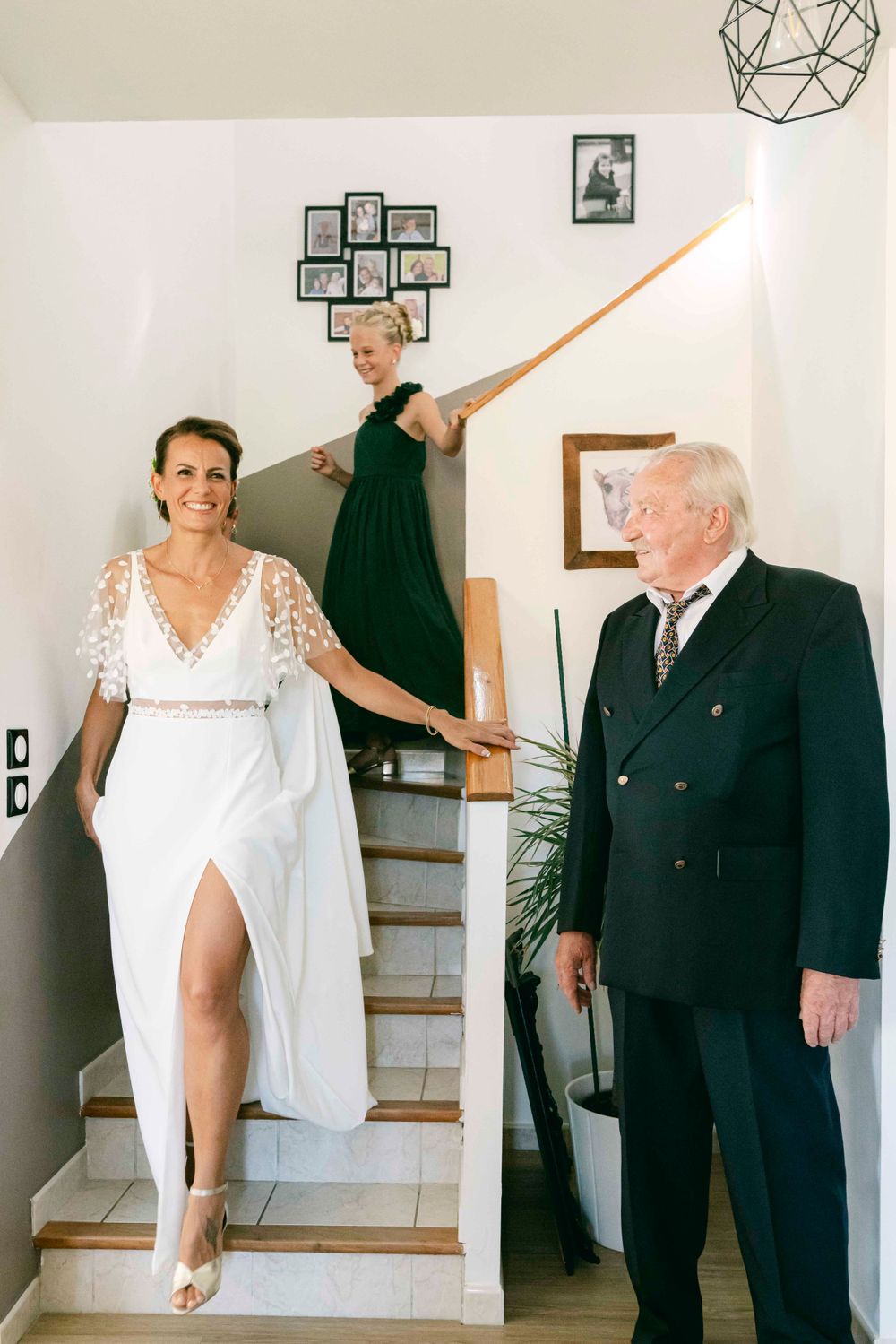 A wedding party gathers on an indoor staircase with elegant decor and family photos on the wall.