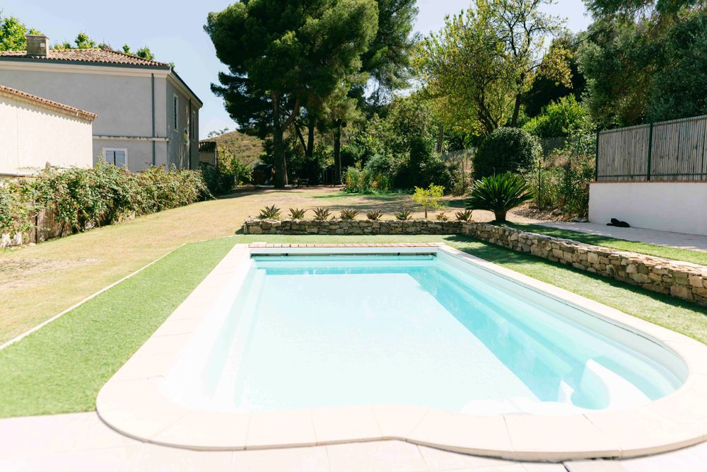 Modern swimming pool with curved edges surrounded by artificial grass in a private backyard setting.