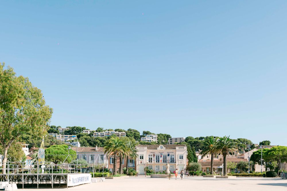 Coastal Mediterranean town with colorful buildings and palm trees under bright blue sky.
