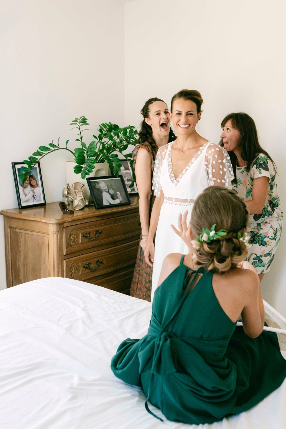 Wedding preparation scene with bridesmaids in green dresses and bride in white lace dress.