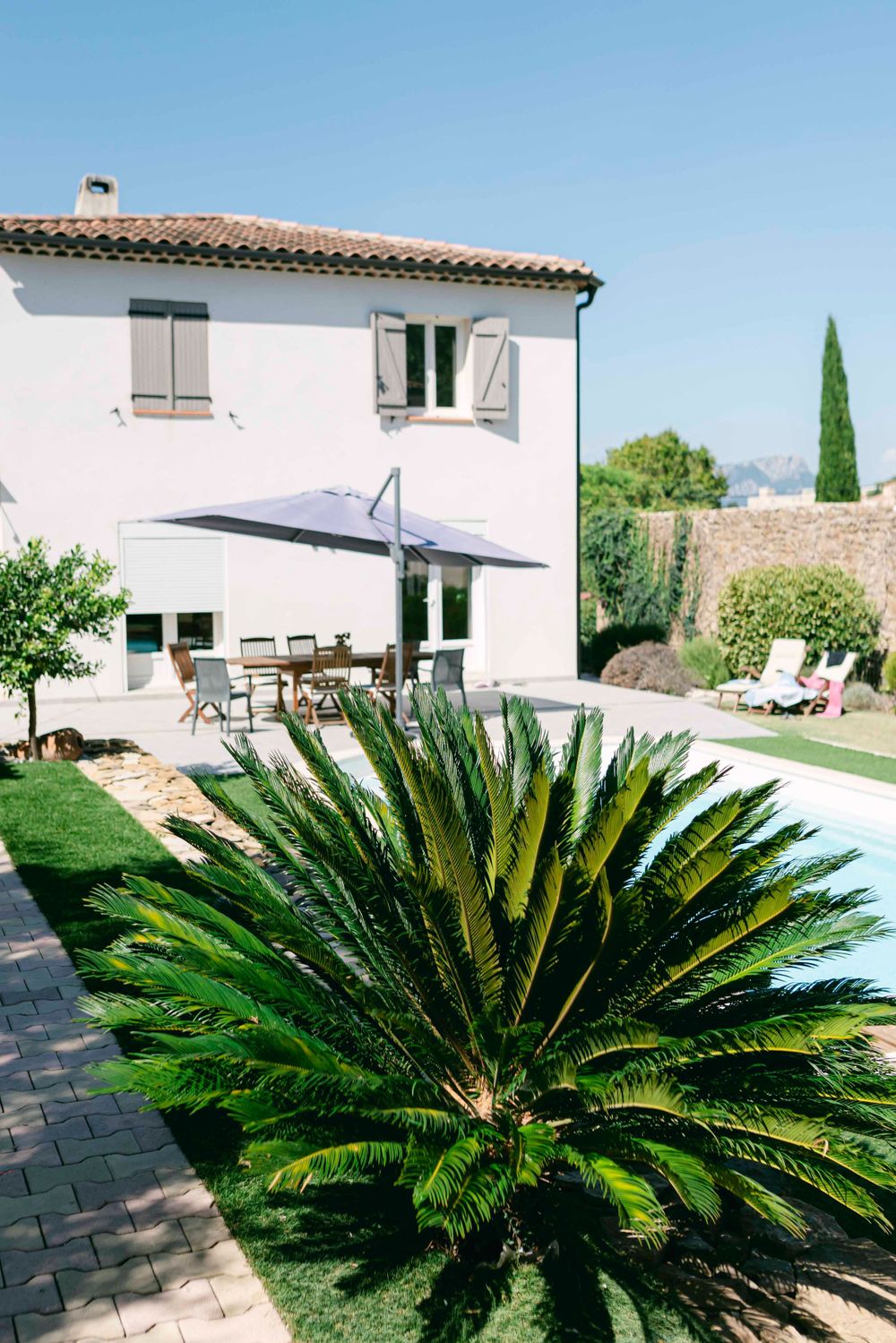Mediterranean-style villa with pink walls, shutters, palm tree, and outdoor patio furniture.