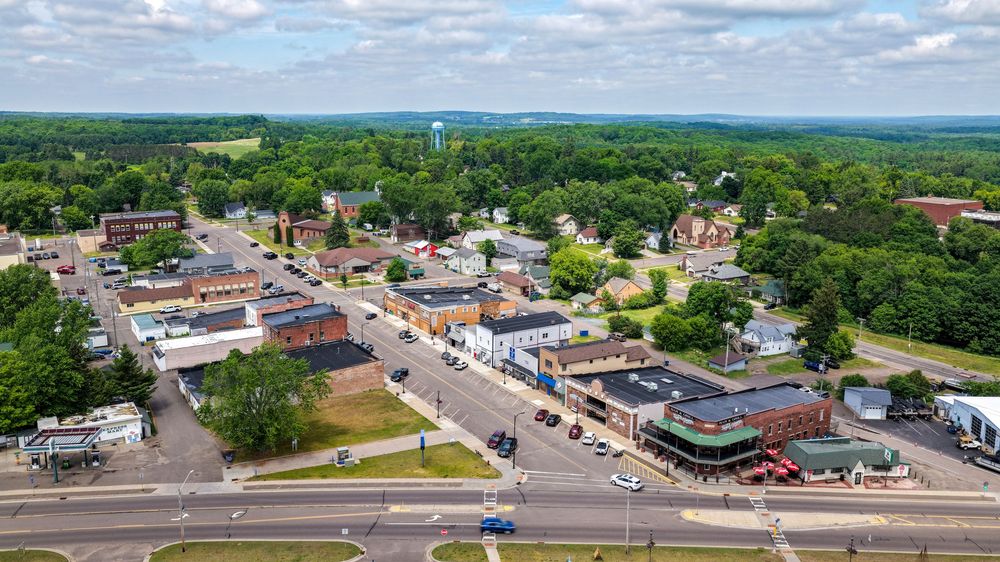 Aerial view of a small town with tree-lined streets, local businesses, and a water tower visible on the horizon.