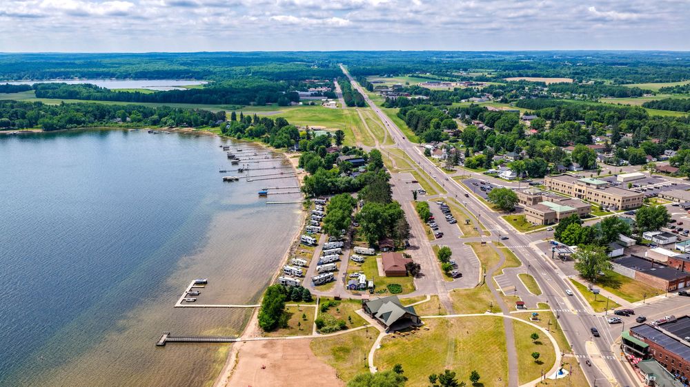 Aerial view of a lakeside town with a marina, sandy shoreline, and a main road running parallel to the water.