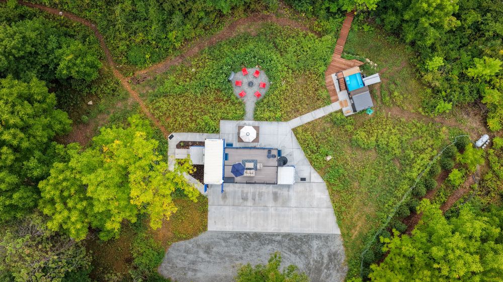Aerial drone view of a secluded property surrounded by lush green forest with a concrete structure and decorative tree feature.