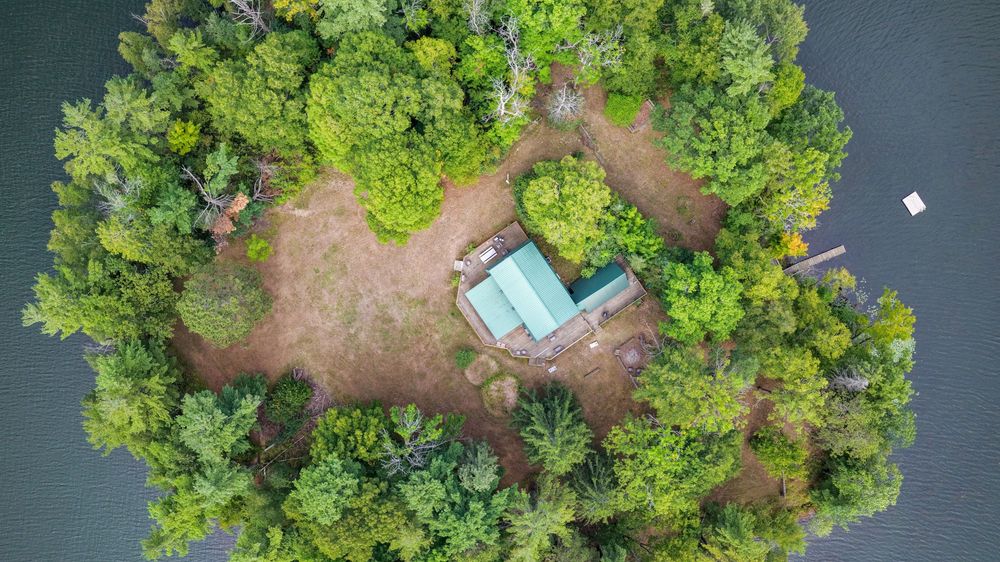 Aerial view of a small wooded island with a cabin and dock surrounded by calm water.