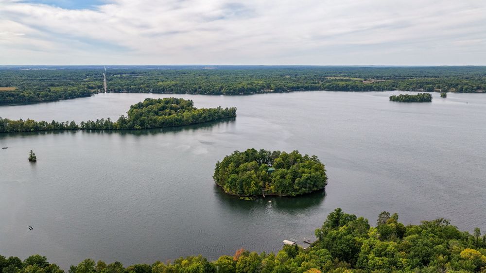 Aerial view of lush green tree-covered islands surrounded by calm blue lake waters under a partly cloudy sky.
