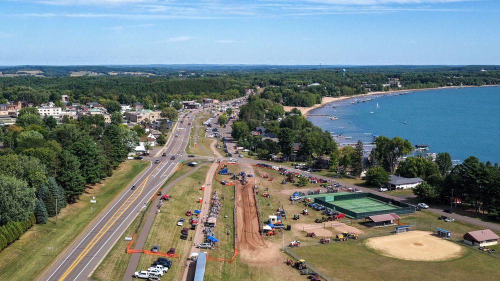 Aerial view of a coastal highway with construction work alongside a sandy beach and lush green trees on a sunny day.