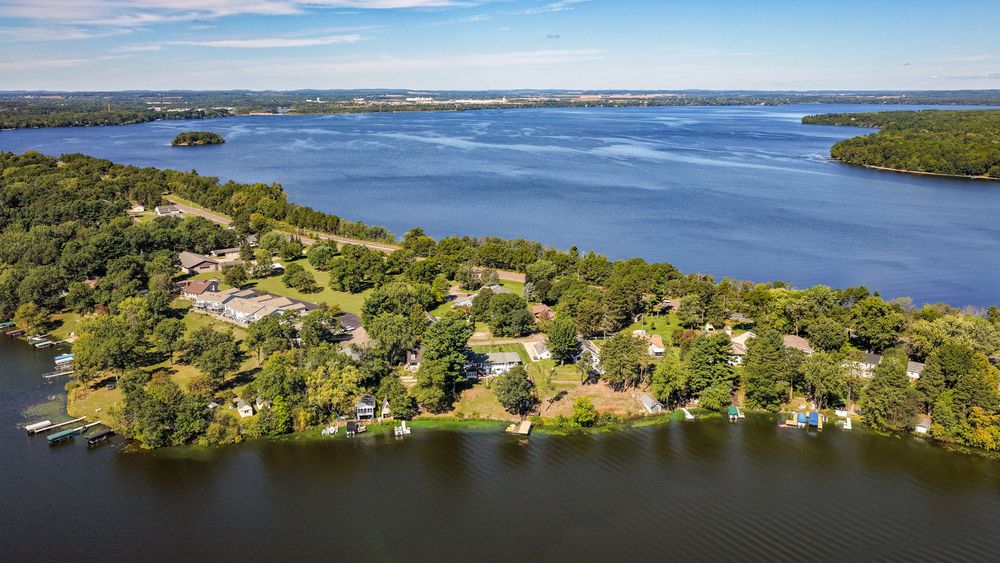 Aerial view of a lush peninsula neighborhood surrounded by calm blue lake waters with docks and dense trees.
