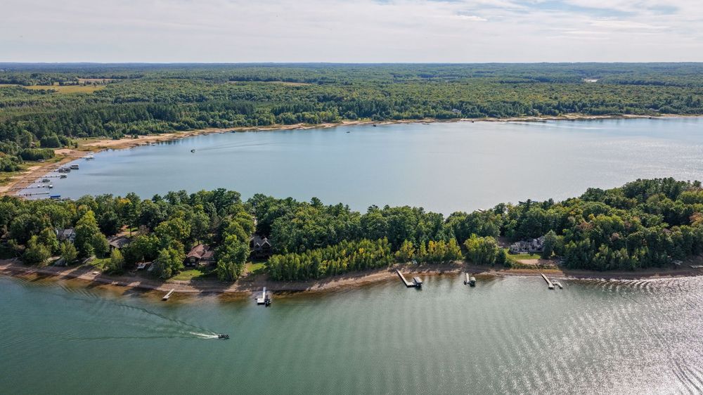 Aerial view of a serene lake surrounded by lush green trees with docks and boats along the shoreline.