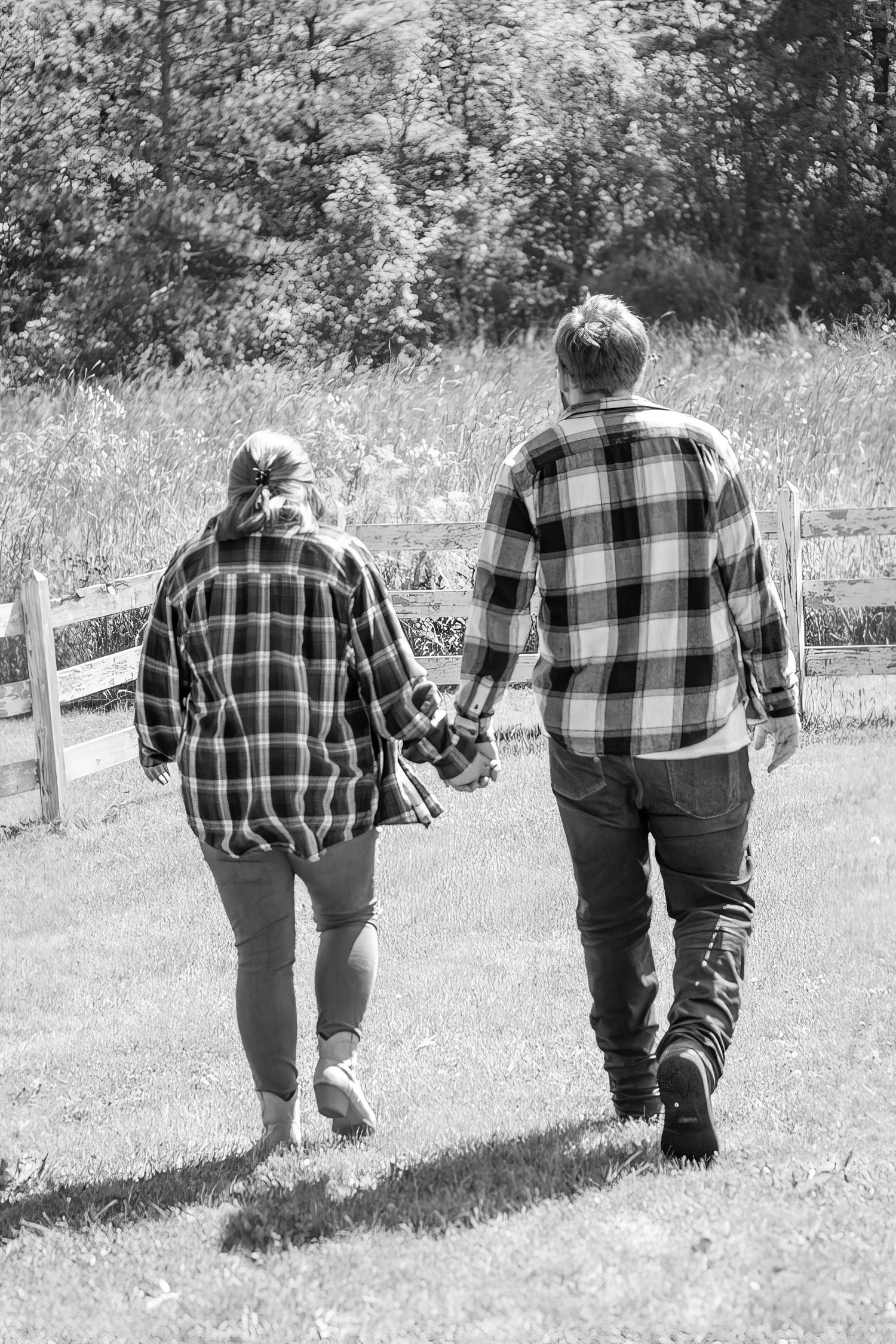 Black and white photo of people walking together in plaid shirts along a fence line.
