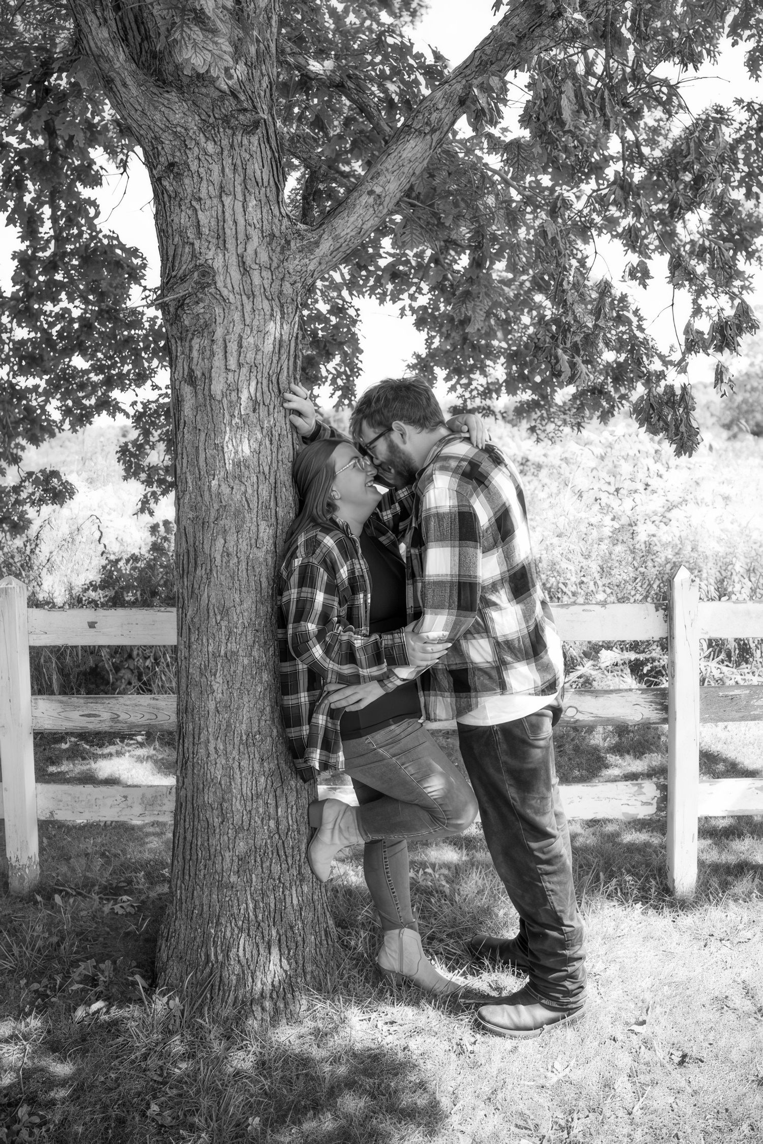 Black and white portrait session among trees with white fence in background.