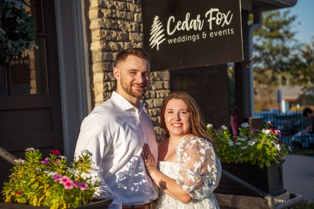 Wedding couple poses outside Cedar Fox lodge with flowers in background.