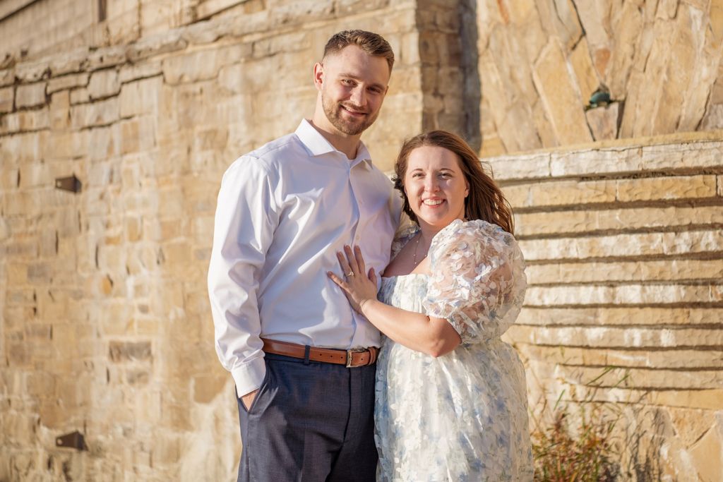 Newlyweds pose together against stone wall with outdoor staircase.
