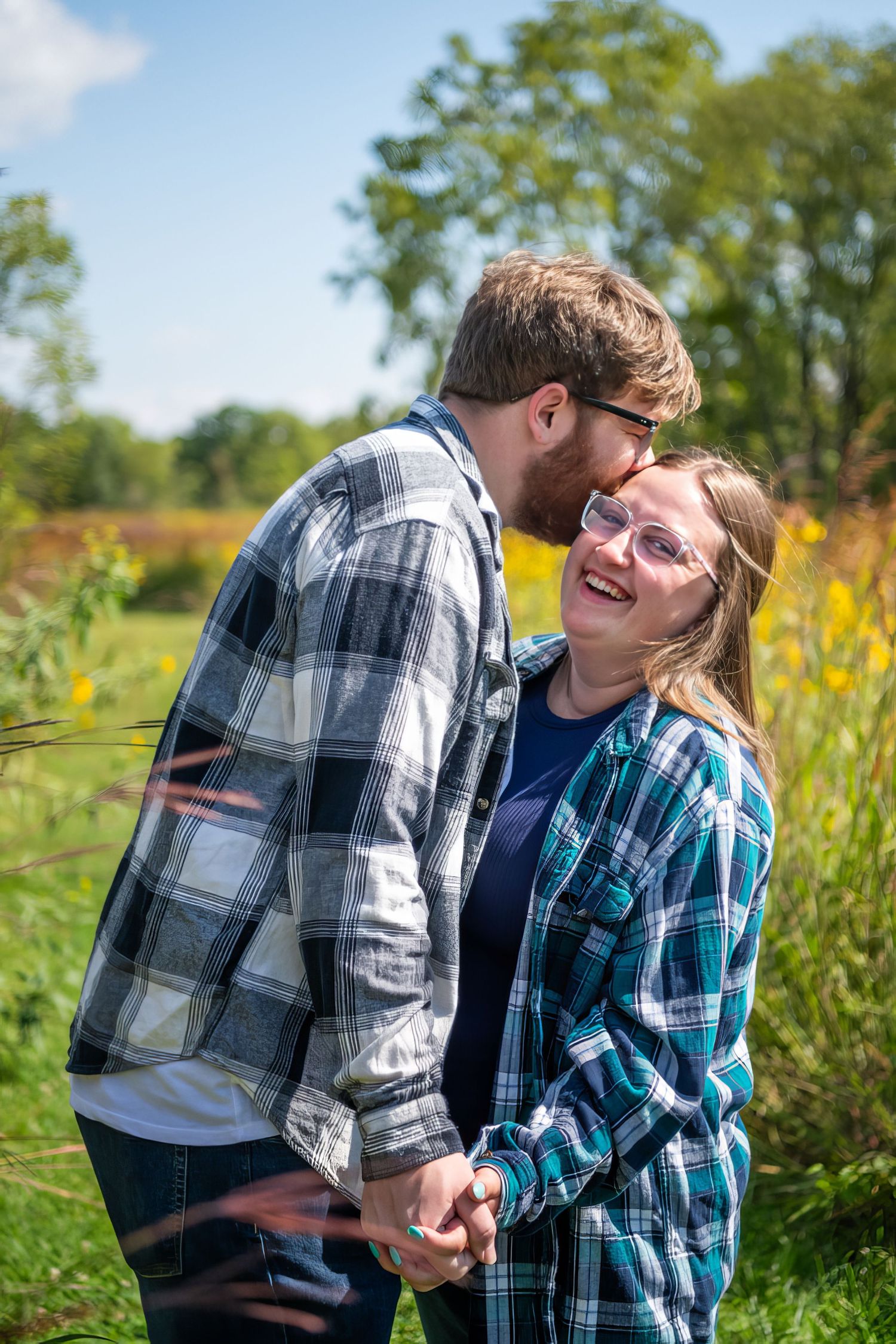 Couple in matching plaid shirts laughing together in a field of yellow wildflowers.