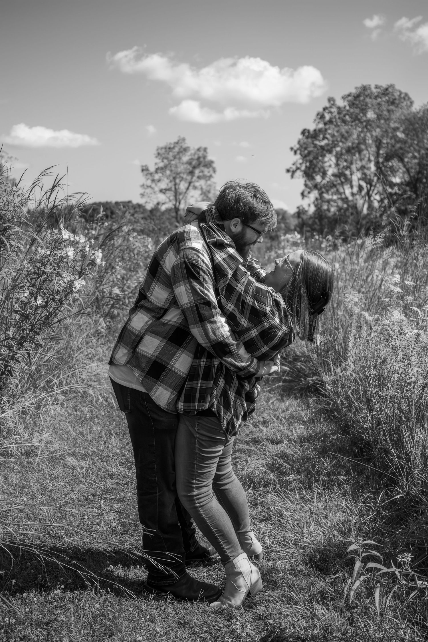People in plaid shirts picking wildflowers in a sunny field.