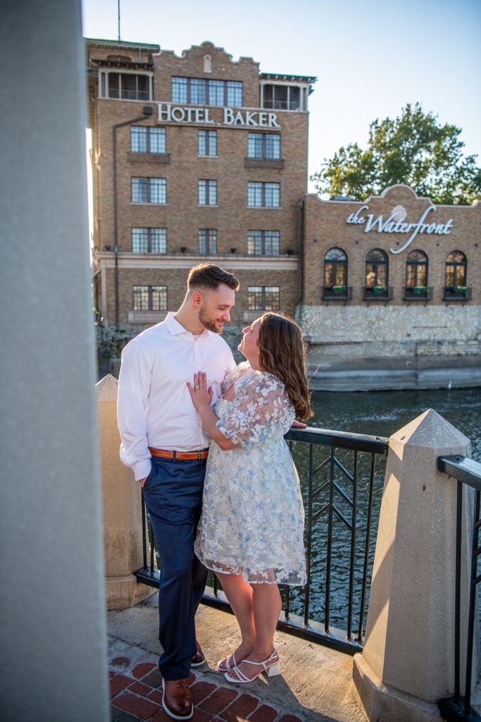 Couple in formal attire poses by Hotel Baker on riverside balcony at sunset.