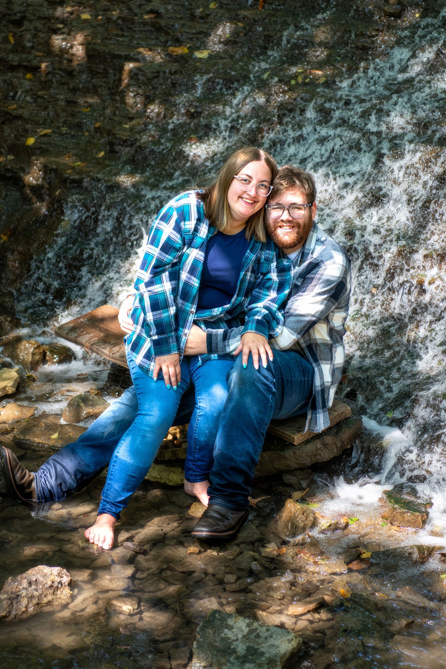 Two people relaxing by a scenic waterfall on moss-covered rocks.