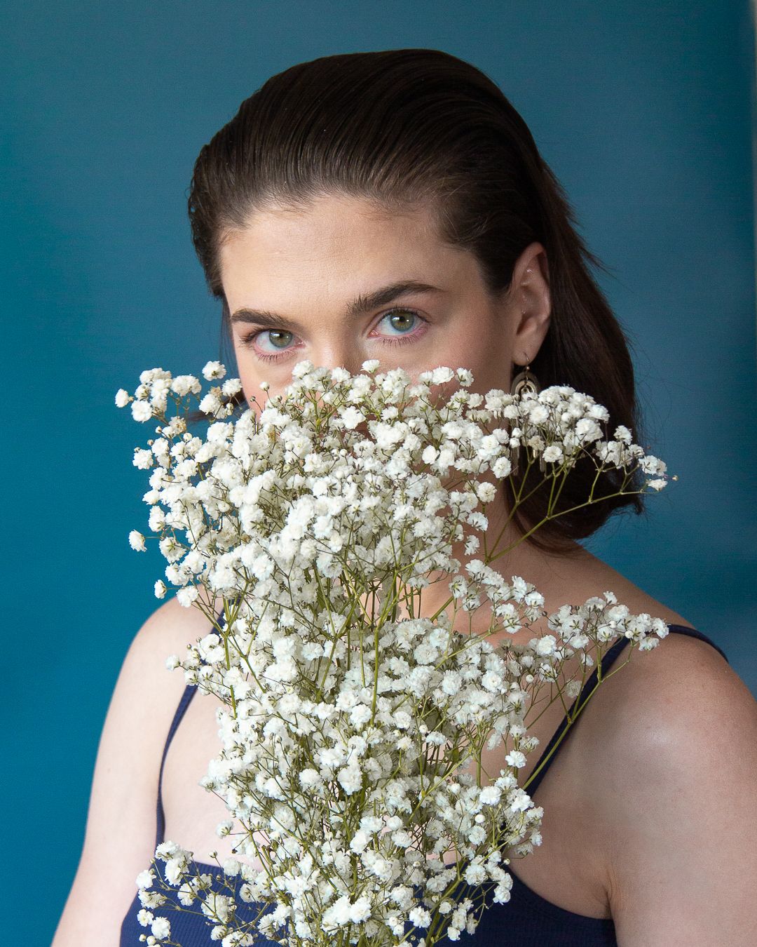 Portrait with baby's breath flowers covering half the face against teal background.