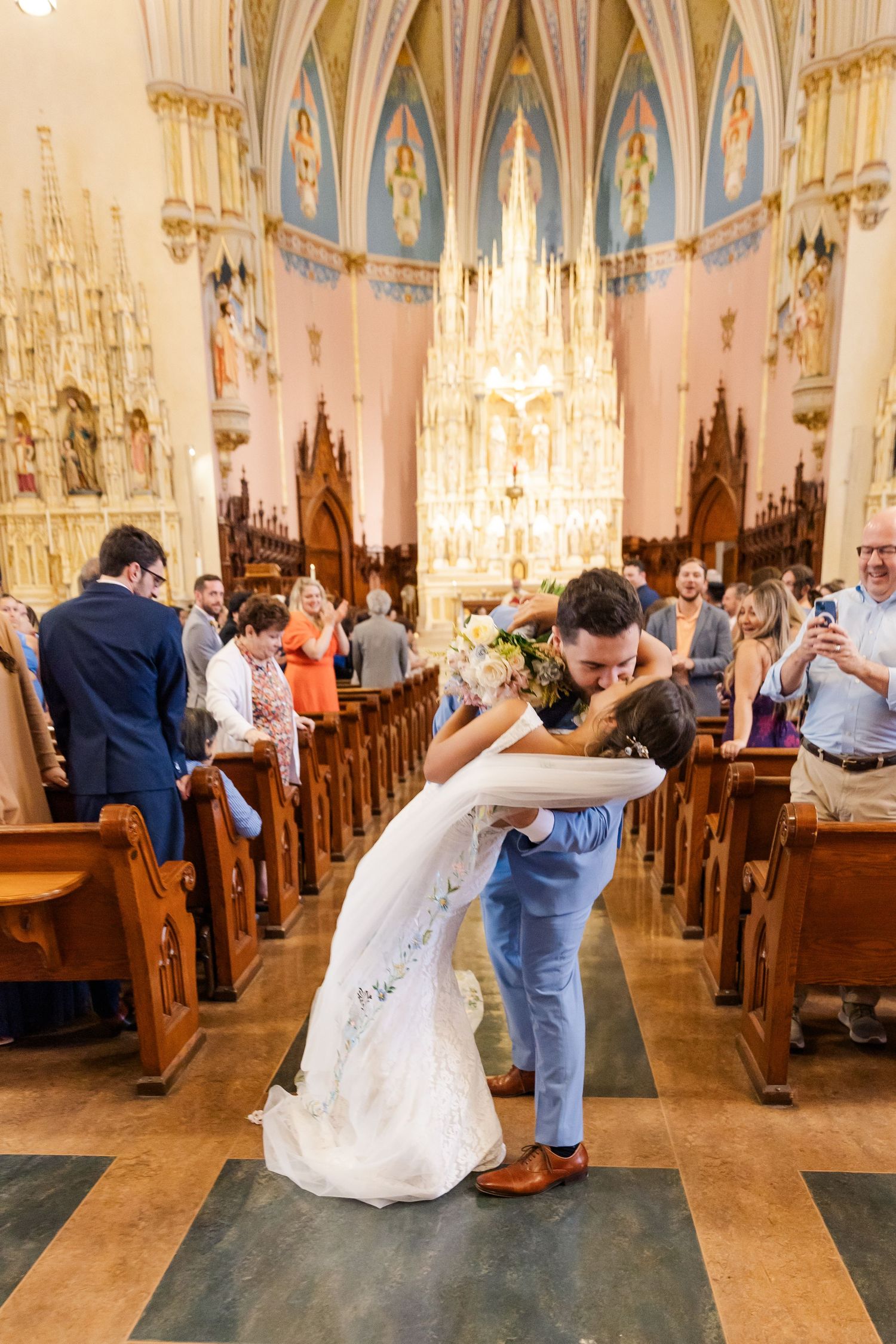A wedding couple share a romantic dance in a stunning cathedral with blue and gold vaulted ceilings and ornate details.