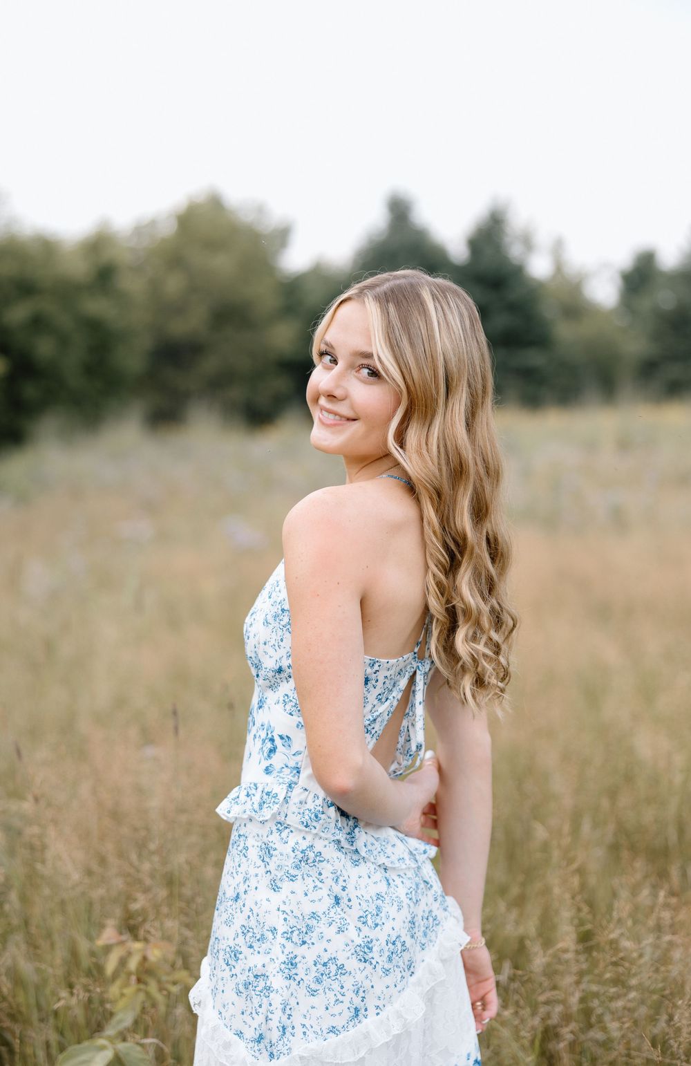 Person in a blue floral dress poses playfully in a summer meadow.