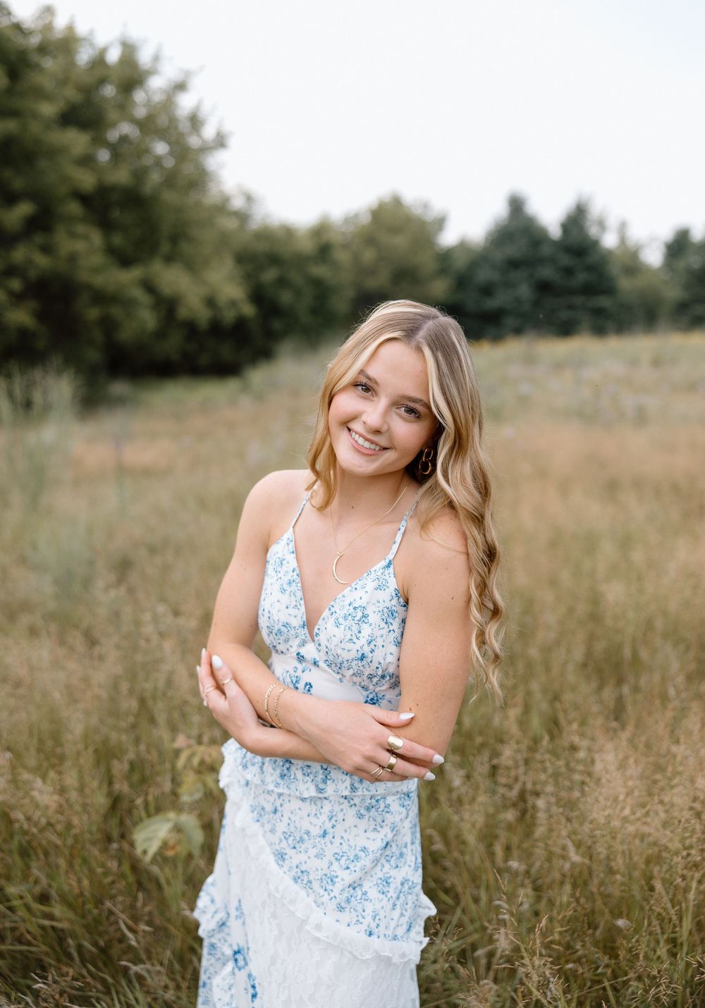 Someone wearing a blue floral dress smiles brightly in a natural field setting.