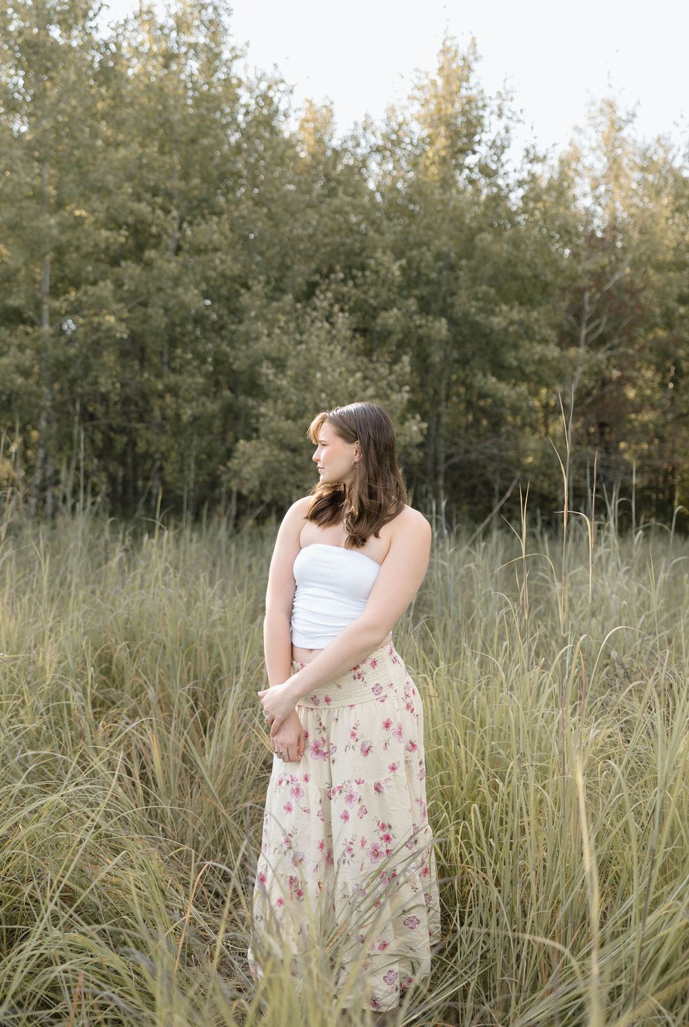 A floral dress sways in a field of tall grass with trees in the background during golden hour.