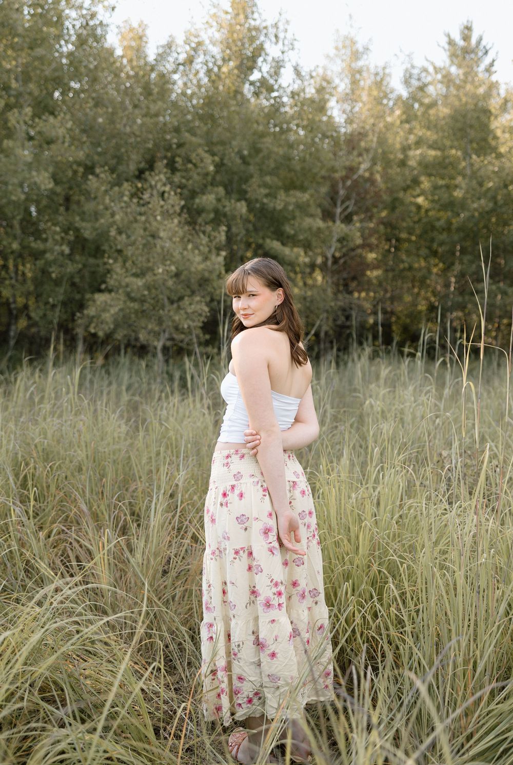 A floral dress sways in a field of tall grass with trees in the background during golden hour.