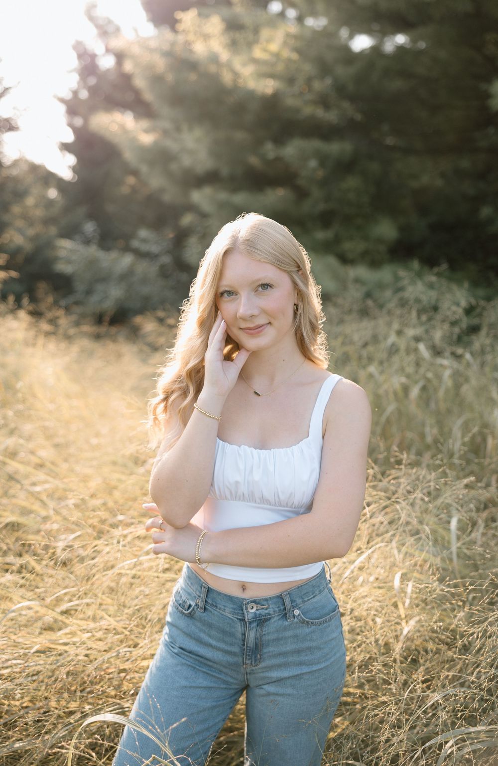 A casual outdoor photoshoot in a golden field at sunset wearing a white crop top and jeans.